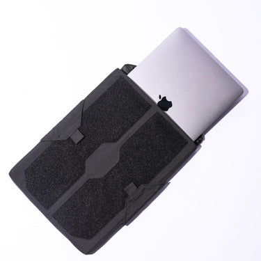Black padded laptop sleeve with hook-and-loop front panel, laptop partially inserted.