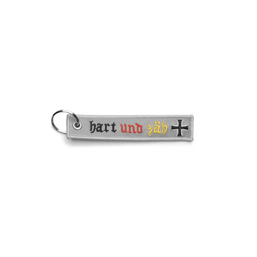 Grey embroidered key ring with 'hart und zäh' text and cross emblem