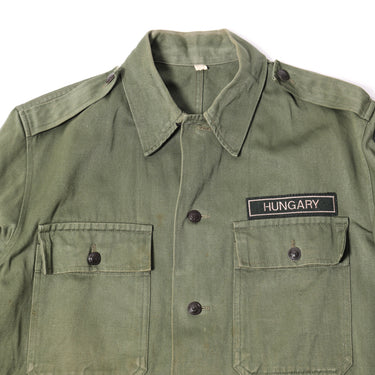 Olive drab field jacket close-up: HUNGARY label, button front, flap pockets