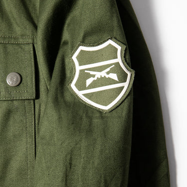 Olive drab jacket sleeve detail with large white shield patch and metal snap