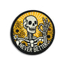 Never Better round embroidered skeleton patch with skull, flowers, and orange burst design