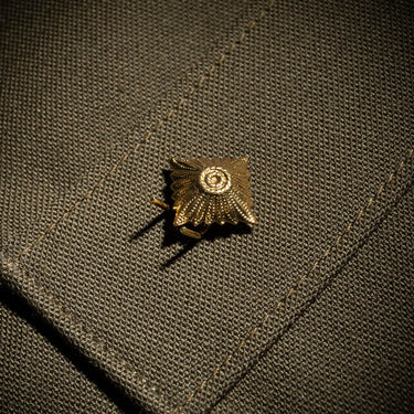 Gold metal star ranking cap badge on dark fabric, circular center and radiating rays