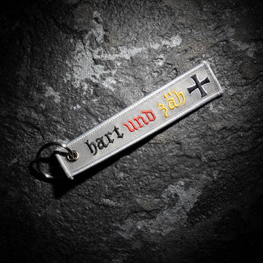 Grey embroidered key ring strap with 'hart und zäh' lettering and cross