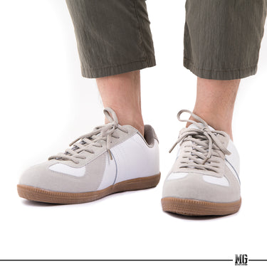 White low-top sneakers on feet with gray pants and tan gum rubber outsoles